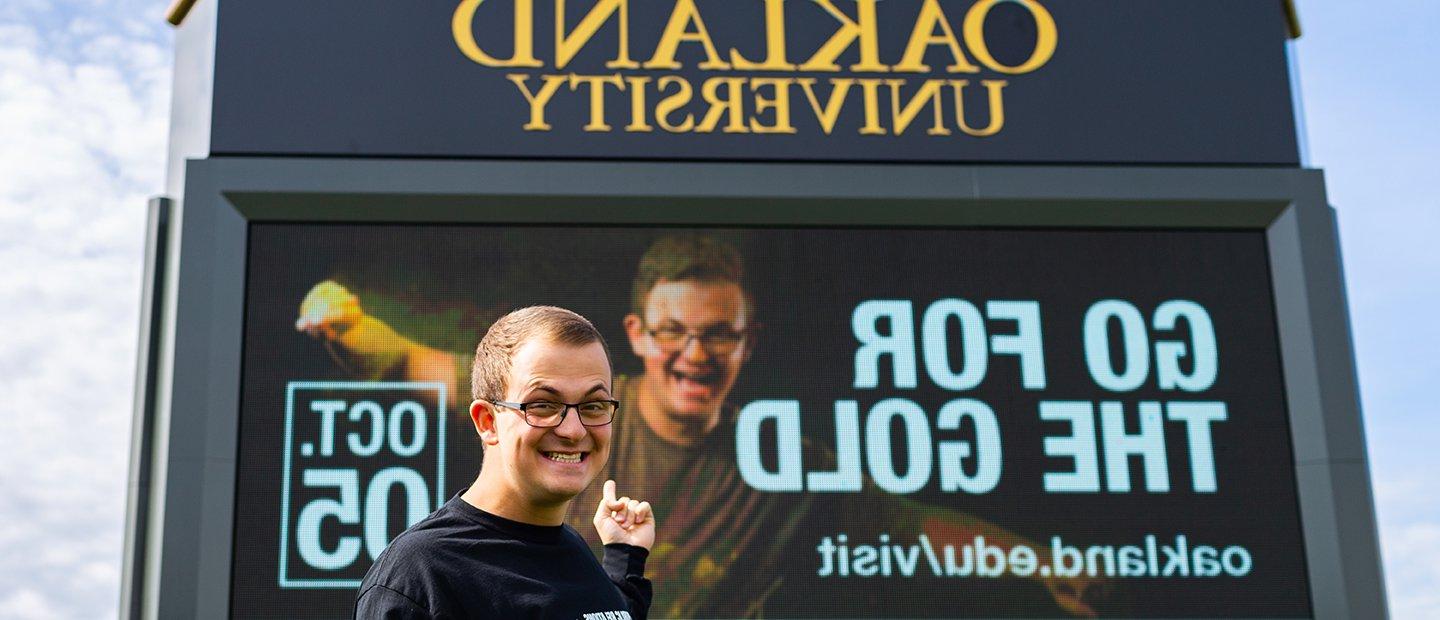 Young man pointing to an ad that he is featured in on an 十大菠菜台子 electronic marquee.
